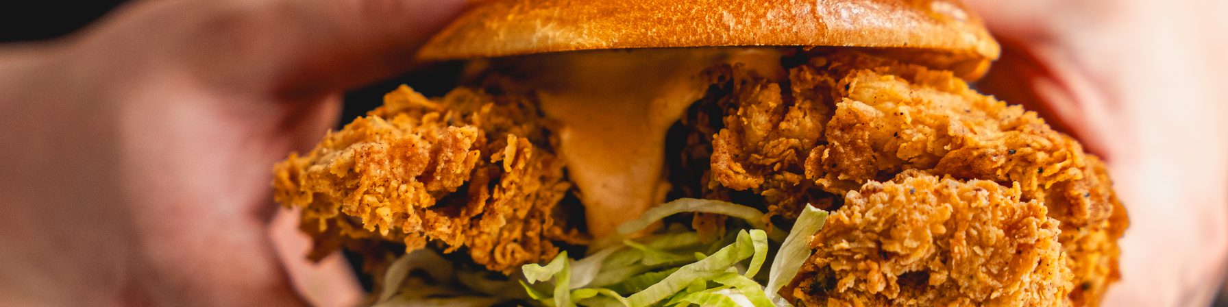 Hands holding a Goldies fried chicken sandwich with sauce and shredded lettuce